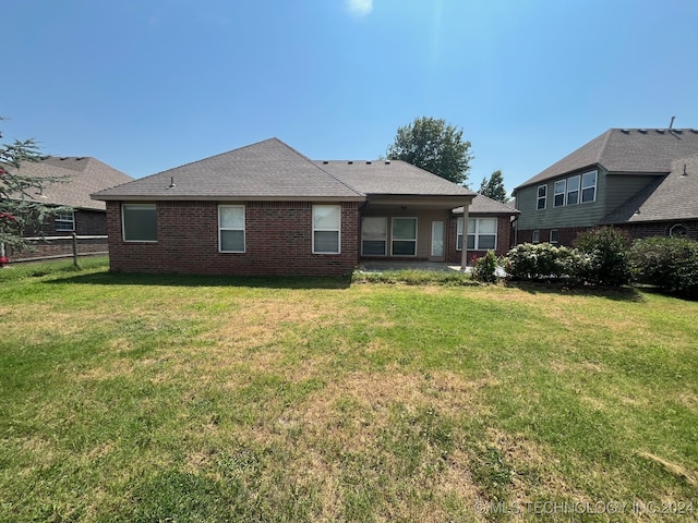 rear view of house with roof with shingles, brick siding, a lawn, and fence