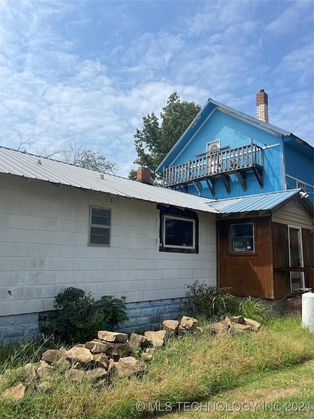 view of home's exterior featuring metal roof, a chimney, and a balcony