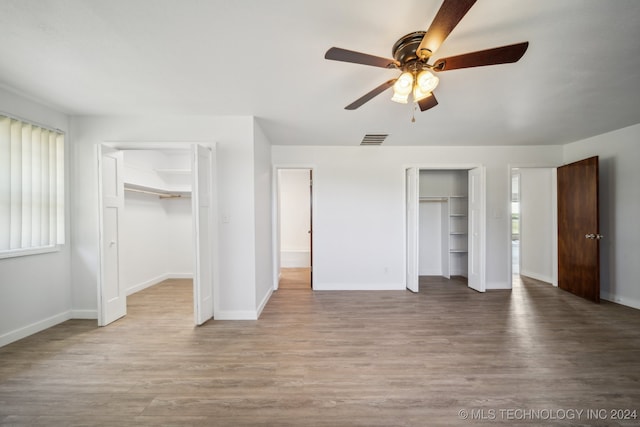 unfurnished bedroom with light wood-type flooring, two closets, and ceiling fan