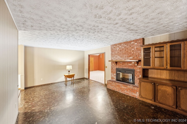 unfurnished living room with wooden walls, brick wall, a textured ceiling, and a brick fireplace