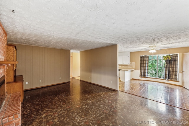 unfurnished living room with ceiling fan, brick wall, a textured ceiling, and a fireplace