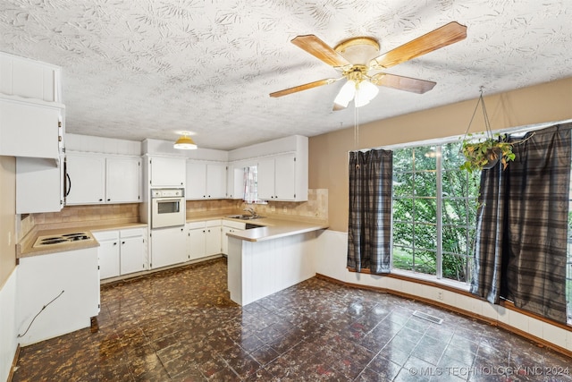 kitchen featuring white oven, plenty of natural light, ceiling fan, and white cabinetry