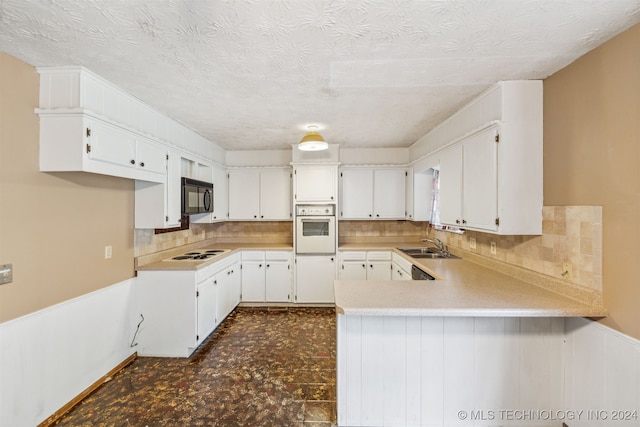 kitchen featuring backsplash, dark tile patterned floors, white cabinetry, kitchen peninsula, and white appliances