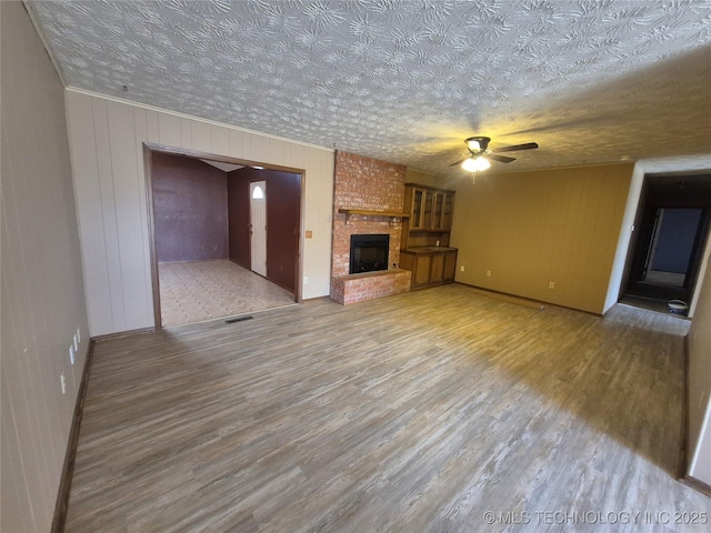 unfurnished living room with visible vents, a brick fireplace, wood finished floors, a textured ceiling, and a ceiling fan