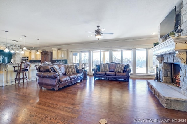 living room featuring ceiling fan, crown molding, a stone fireplace, and dark hardwood / wood-style floors