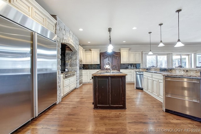 kitchen featuring light hardwood / wood-style flooring, tasteful backsplash, an island with sink, appliances with stainless steel finishes, and light stone counters