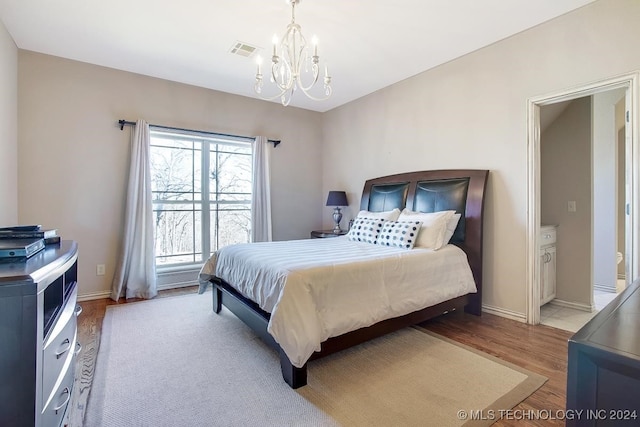 bedroom with an inviting chandelier, ensuite bathroom, and light hardwood / wood-style flooring