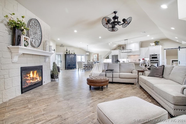 living room with light wood-type flooring, vaulted ceiling, a barn door, and a tile fireplace