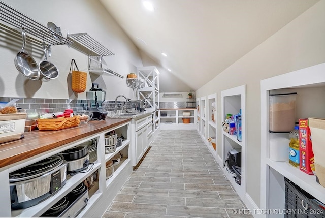 interior space with wood counters, tasteful backsplash, vaulted ceiling, white cabinetry, and sink