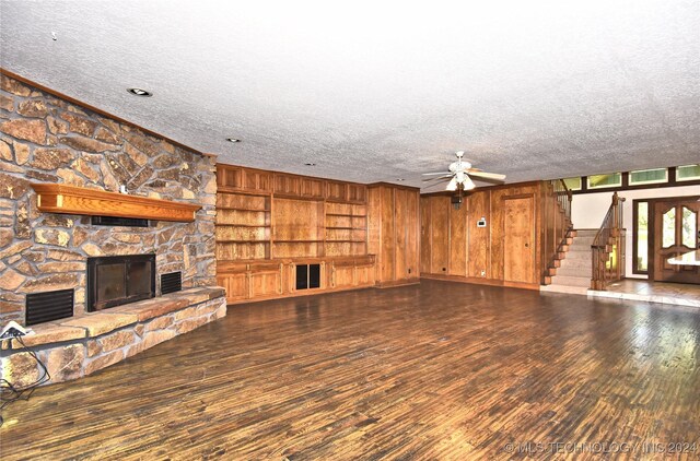 unfurnished living room with stairway, a ceiling fan, a stone fireplace, a textured ceiling, and wood finished floors