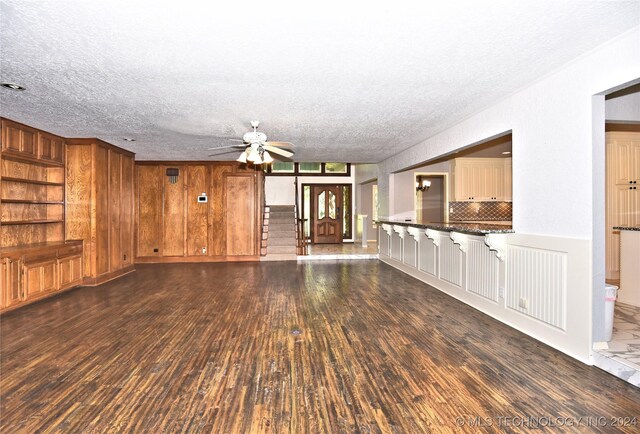 unfurnished living room with dark hardwood / wood-style flooring, a textured ceiling, ceiling fan, and built in shelves