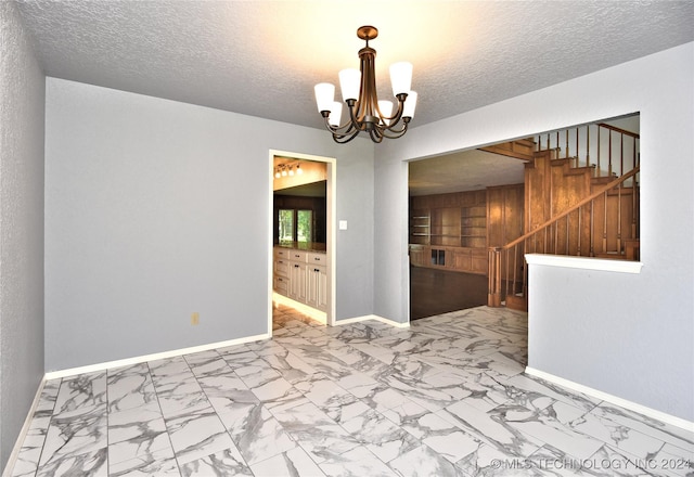 empty room featuring marble finish floor, an inviting chandelier, a textured ceiling, baseboards, and stairs