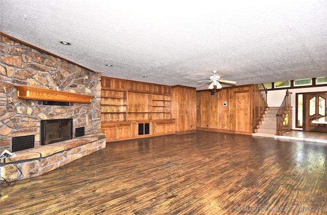 unfurnished living room featuring a stone fireplace, dark hardwood / wood-style flooring, built in shelves, a textured ceiling, and ceiling fan