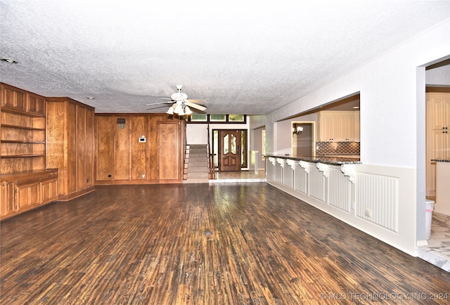 unfurnished living room with ceiling fan, a textured ceiling, built in features, and dark hardwood / wood-style flooring