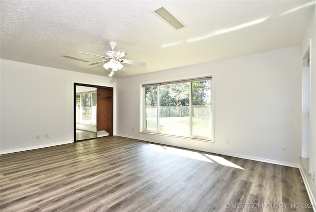 unfurnished room with a textured ceiling, wood finished floors, visible vents, and baseboards