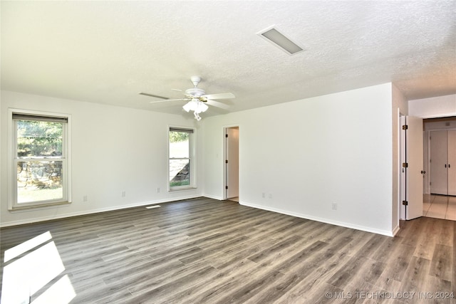 unfurnished room with a textured ceiling, wood finished floors, a wealth of natural light, and baseboards