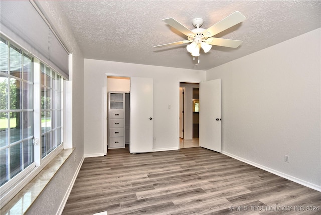 unfurnished bedroom featuring a textured ceiling, multiple windows, wood finished floors, and baseboards