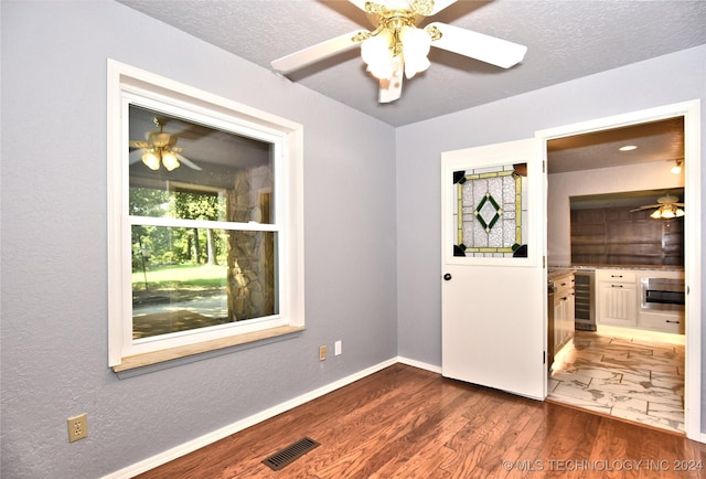 unfurnished room with beverage cooler, baseboards, visible vents, wood finished floors, and a textured ceiling