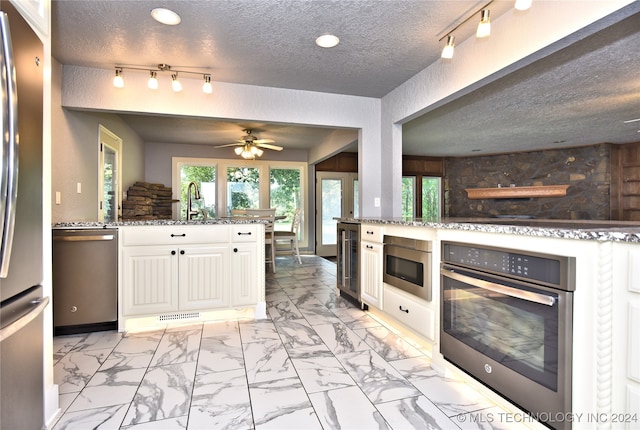 kitchen with white cabinetry, a textured ceiling, light stone counters, and stainless steel appliances