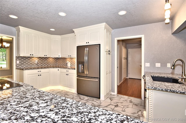 kitchen with a sink, marble finish floor, stainless steel fridge with ice dispenser, tasteful backsplash, and dark stone countertops