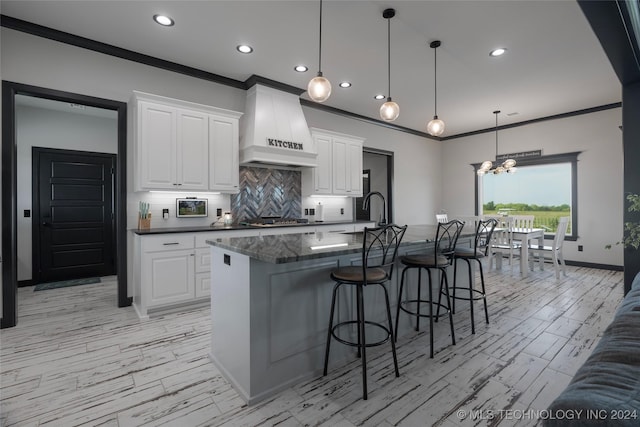 kitchen featuring white cabinets, a large island with sink, premium range hood, and pendant lighting