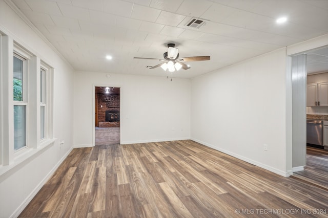 empty room with a fireplace, dark wood-type flooring, and ceiling fan