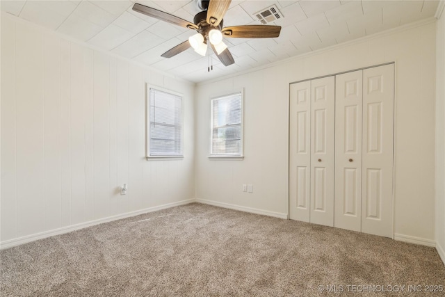 unfurnished bedroom with a ceiling fan, crown molding, a closet, carpet floors, and visible vents