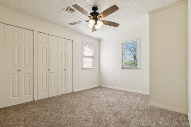 unfurnished bedroom featuring a ceiling fan, crown molding, multiple closets, carpet, and visible vents