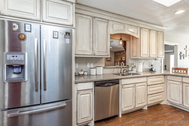 kitchen with sink, appliances with stainless steel finishes, dark wood-type flooring, cream cabinets, and a textured ceiling