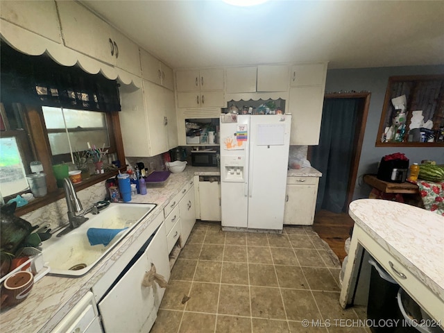 kitchen featuring white fridge with ice dispenser, tile patterned flooring, white cabinets, and sink