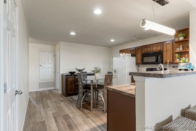 kitchen with kitchen peninsula, decorative light fixtures, white fridge with ice dispenser, and light hardwood / wood-style floors