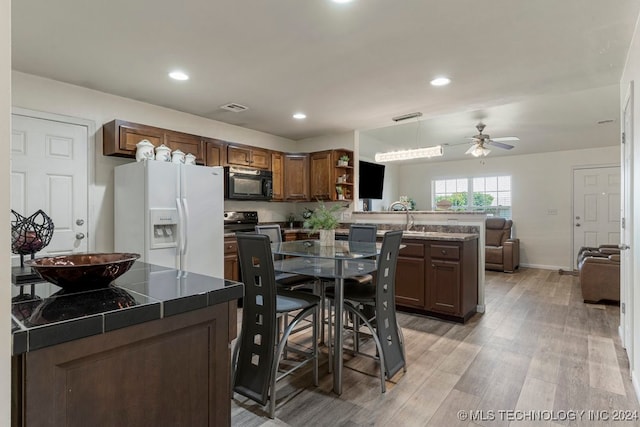 kitchen featuring ceiling fan, light hardwood / wood-style flooring, white fridge with ice dispenser, decorative light fixtures, and kitchen peninsula