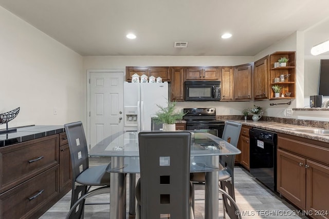 kitchen featuring sink, light hardwood / wood-style floors, black appliances, and tile counters