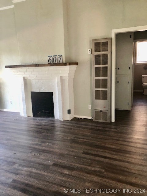 unfurnished living room with dark wood-type flooring and a brick fireplace