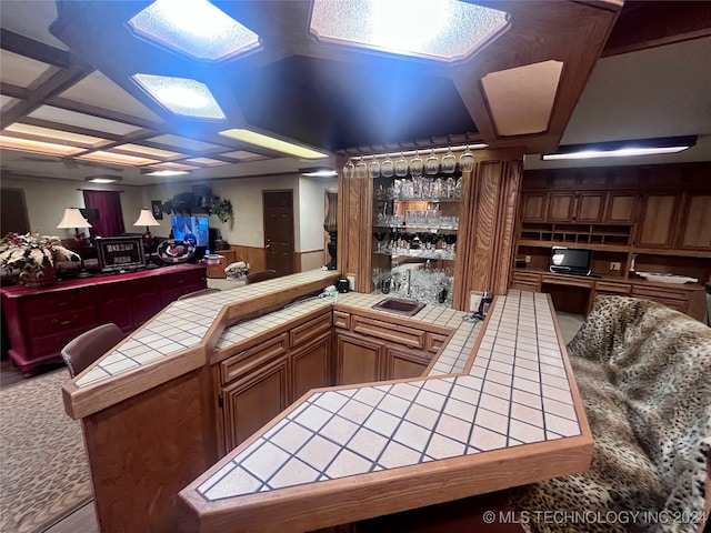 bar featuring tile countertops, coffered ceiling, and sink