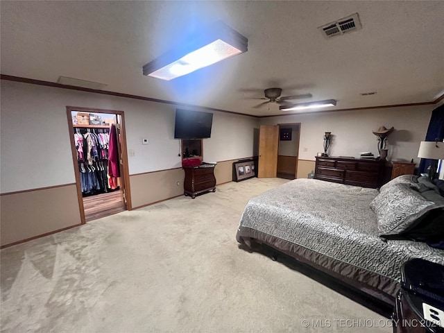 carpeted bedroom featuring a closet, ornamental molding, ceiling fan, and a walk in closet