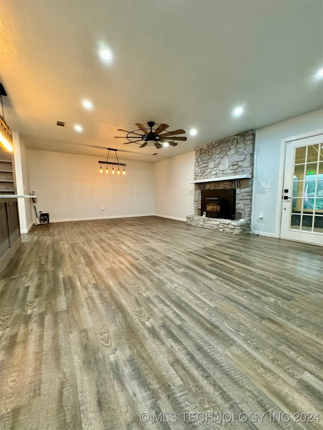 unfurnished living room featuring ceiling fan, hardwood / wood-style floors, and a stone fireplace