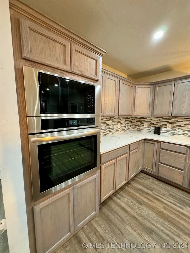 kitchen with light brown cabinets, light hardwood / wood-style flooring, backsplash, and oven