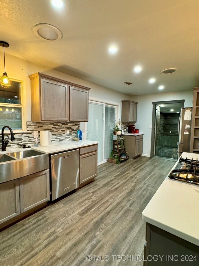 kitchen featuring light wood-type flooring, decorative backsplash, hanging light fixtures, sink, and stainless steel appliances