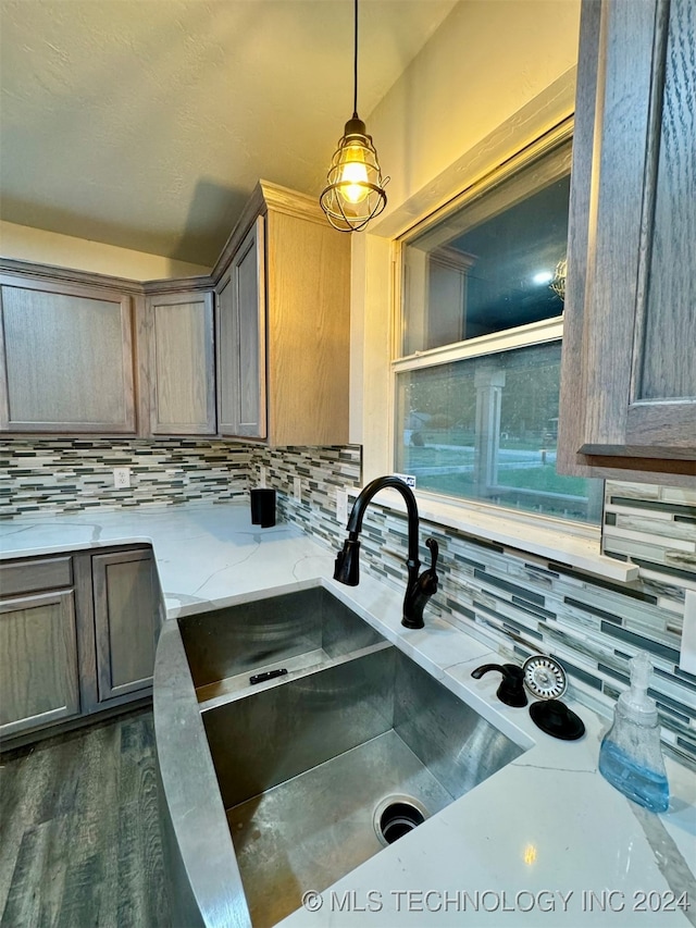 kitchen with sink, dark wood-type flooring, decorative backsplash, light stone countertops, and pendant lighting