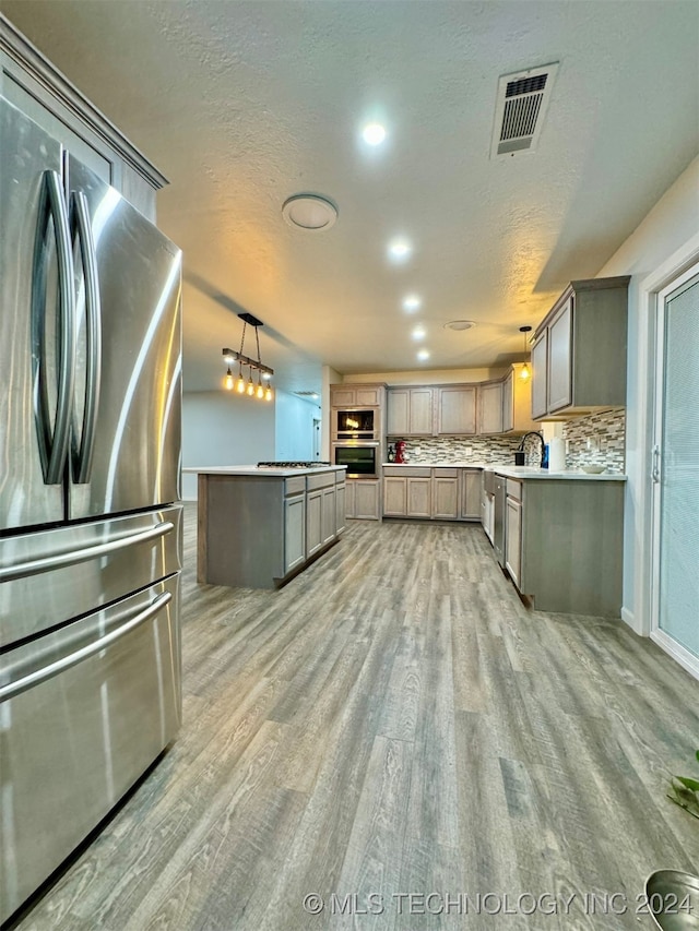 kitchen with backsplash, stainless steel appliances, pendant lighting, and hardwood / wood-style floors