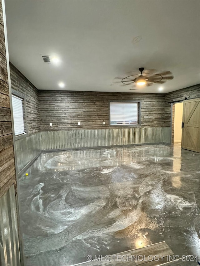 basement with ceiling fan, a barn door, and a healthy amount of sunlight