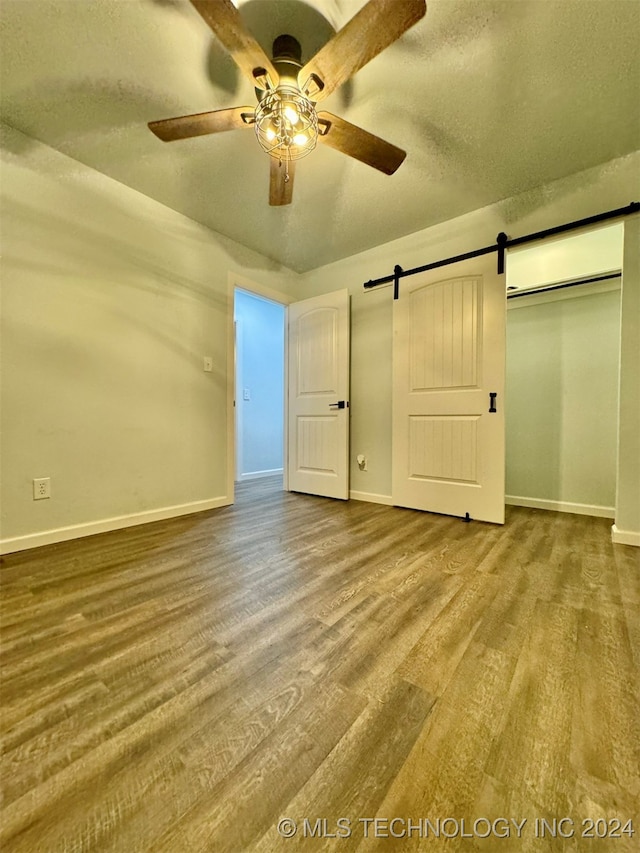 unfurnished bedroom featuring ceiling fan, a closet, a barn door, and hardwood / wood-style floors