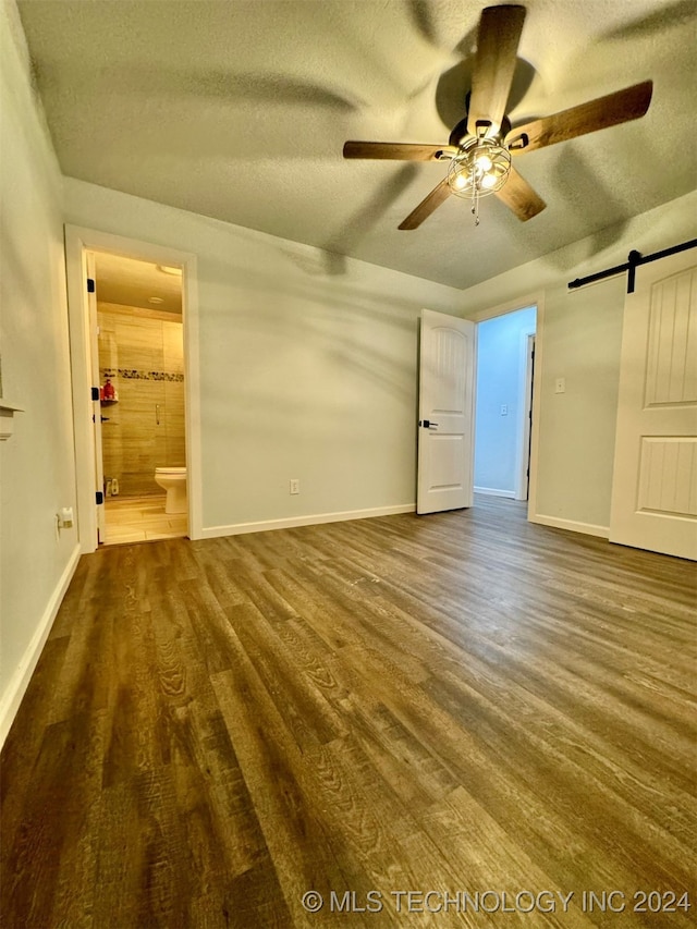 unfurnished bedroom with ceiling fan, connected bathroom, a barn door, and dark wood-type flooring