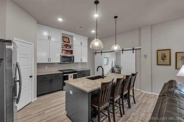 kitchen featuring a barn door, light wood-type flooring, appliances with stainless steel finishes, white cabinetry, and decorative backsplash