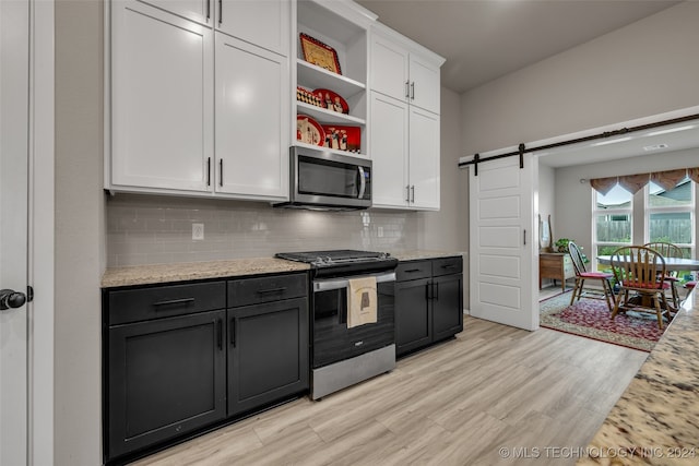 kitchen featuring light wood-type flooring, white cabinetry, decorative backsplash, appliances with stainless steel finishes, and a barn door