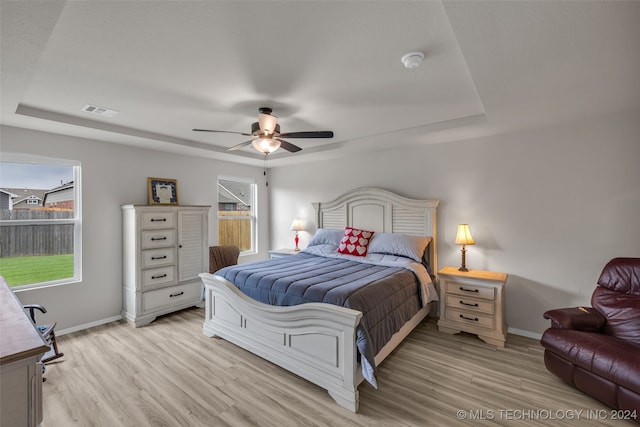 bedroom featuring ceiling fan, a raised ceiling, and light hardwood / wood-style floors