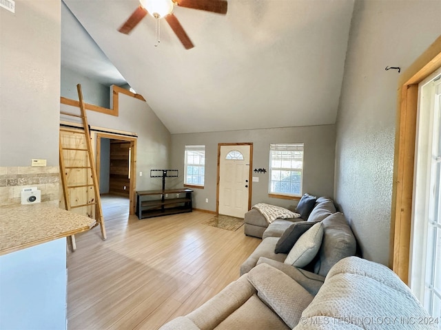 living room featuring light hardwood / wood-style floors, a barn door, high vaulted ceiling, and ceiling fan