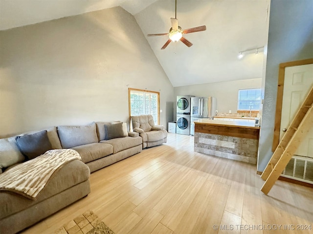 living room featuring light hardwood / wood-style flooring, stacked washer and clothes dryer, high vaulted ceiling, and ceiling fan