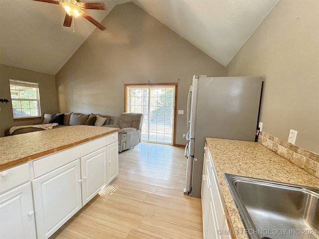 kitchen with a wealth of natural light, white cabinetry, high vaulted ceiling, and stainless steel refrigerator